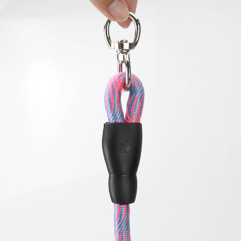 Hand, die einen Karabiner hält, der an einer rosa-blauen Hundeleine mit schwarzem Gummigriffgriff gegen einen einfachen weißen Hintergrund befestigt ist.