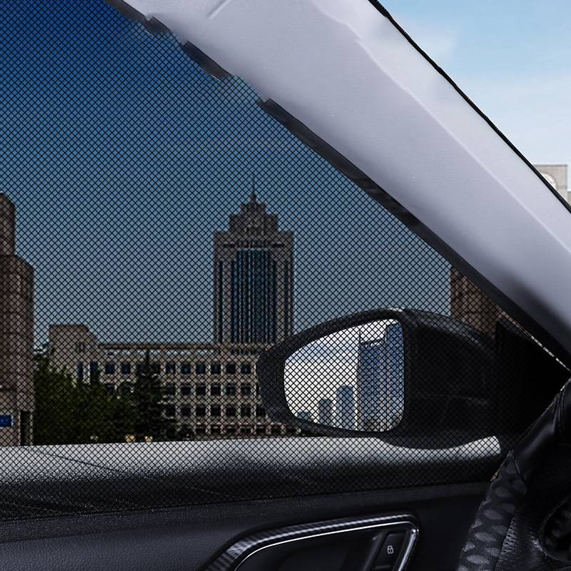Blick durch ein Auto-Seitenfenster mit Sonnenschutzgitter, das Stadtgebäude und Skyline zeigt, einschließlich des Seitenspiegels und des Auto-Türinneren.