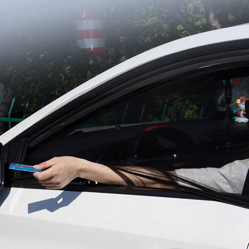 Hand, die aus einem Autofenster eines weißen Autos herausgestreckt wird und eine blaue Karte gegen einen Seitenspiegel hält, als würde sie bei einem Drive-Through oder an einer Mautstelle bezahlen oder ein Ticket vorzeigen.