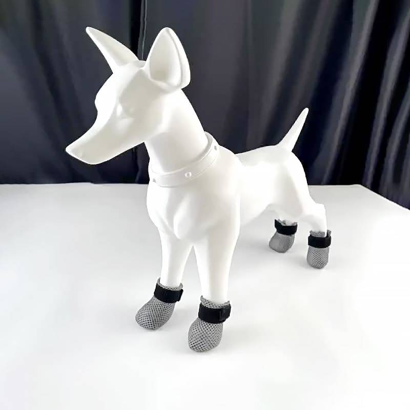 Weiße Hundefigur, die auf einer Tischplatte steht, mit vier grauen Mesh-Pfotenschutzern und schwarzen Riemen.