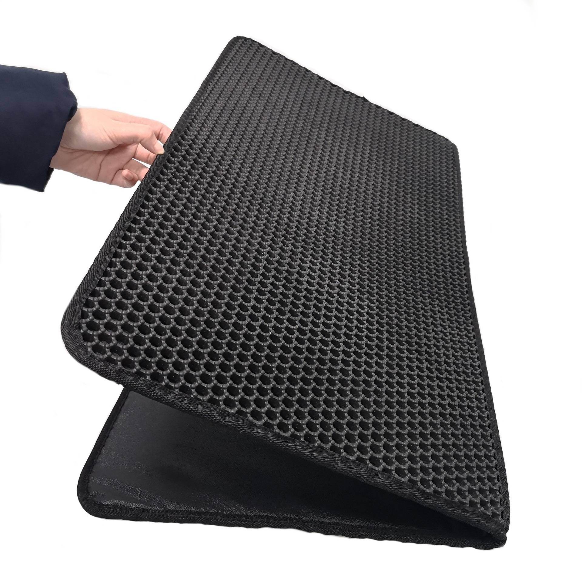 Hand hält eine schwarze strukturierte Gummimatte mit Wabenmuster, gefaltet, um Dicke und Rückseite auf weißem Hintergrund zu zeigen.