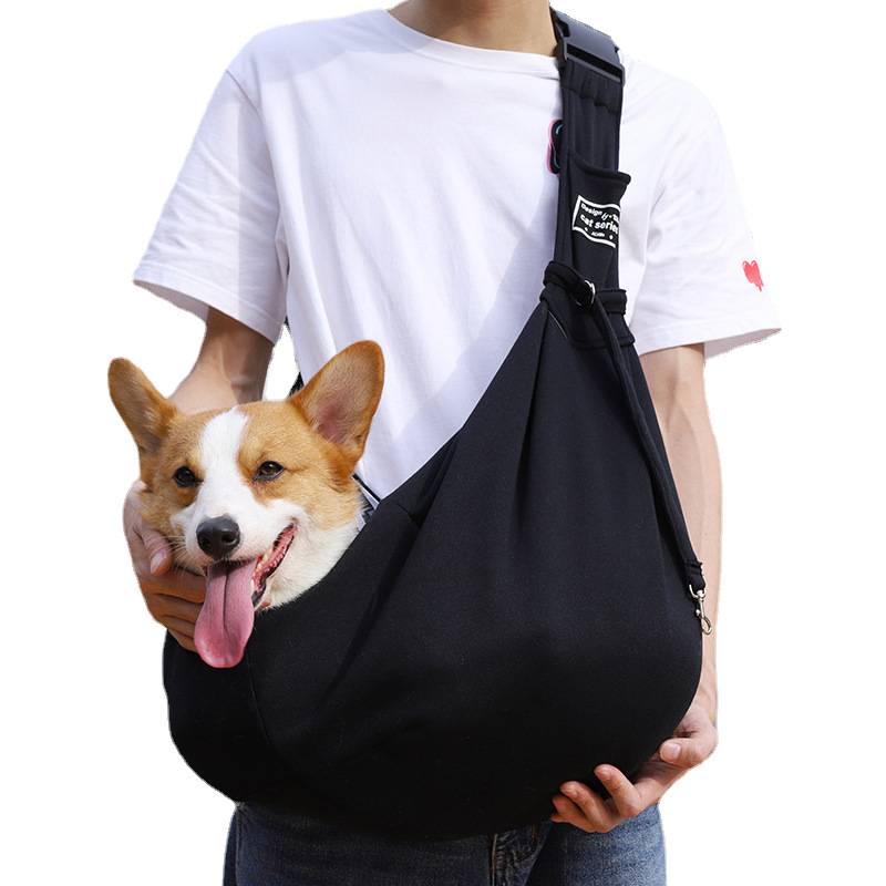 Eine Person trägt einen Corgi in einer schwarzen Umhänge-Transporttasche für Haustiere über der Brust, wobei der Kopf des Hundes außerhalb ruht.