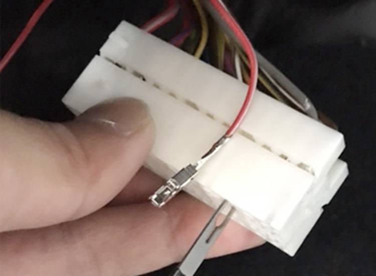 Nahaufnahme einer Hand, die einen weißen kunststoffgestrickten elektrischen Stecker mit mehreren farbigen Drähten hält.