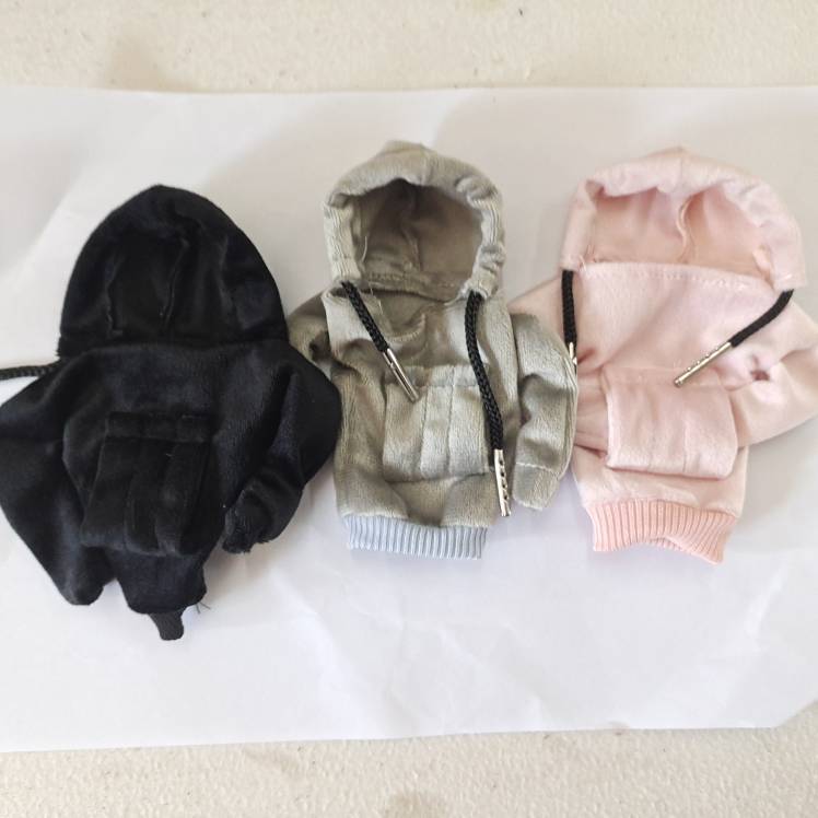 Drei kleine Kapuzen-Reißverschluss-Haustiersweater nebeneinander in Schwarz, Grau und Rosa auf einer weißen Oberfläche.
