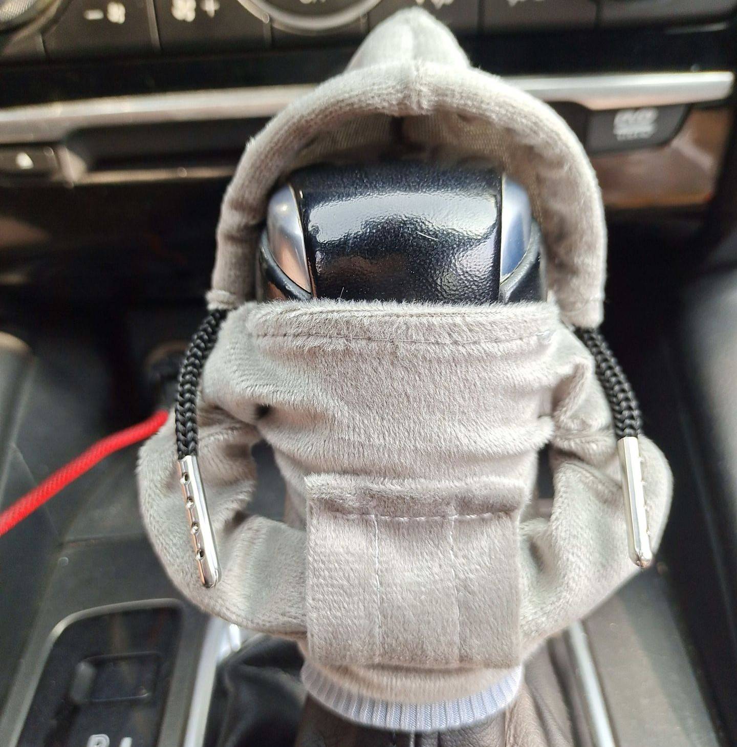 Ein Schalthebel-Knauf, eingewickelt in einen grauen Schutzbeutel mit Zugschnur, in einer Autokonsole.