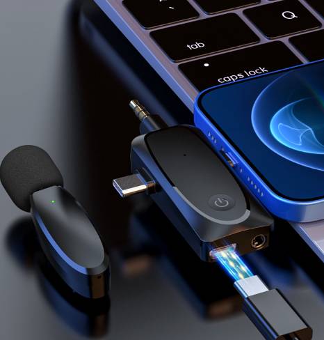 Smartphone, das an einen USB-C-Multiadapter angeschlossen ist, neben einem Laptop, mit einem kabellosen Kopfhörer und Ladekabel auf einer dunklen Oberfläche.