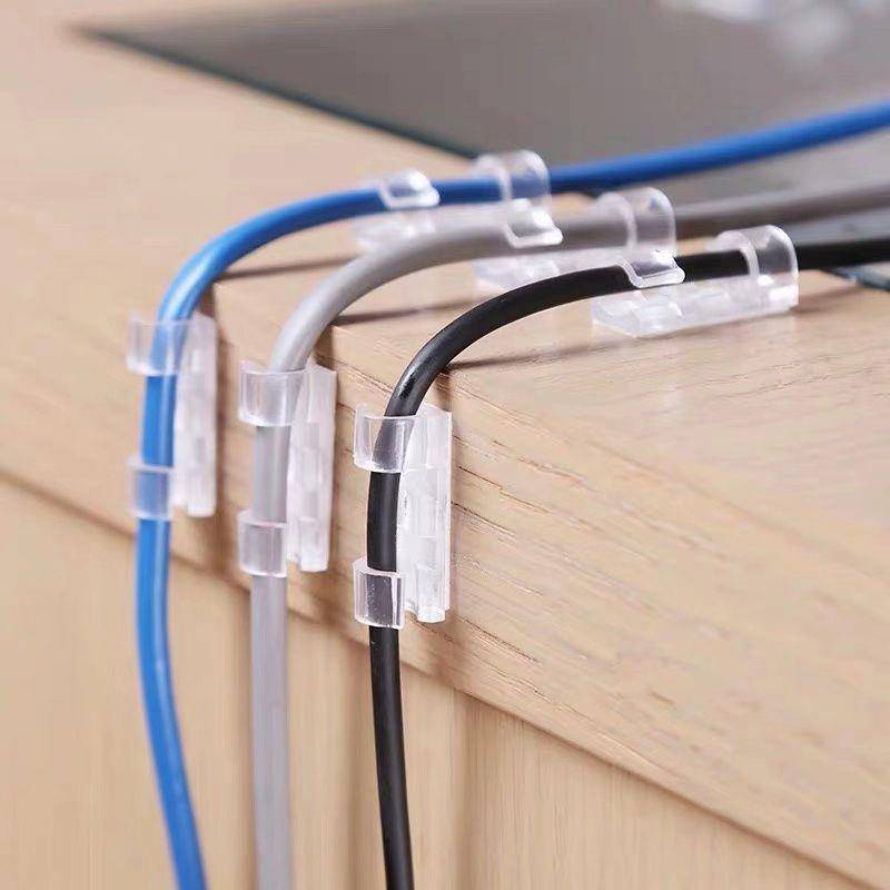 Kabelclips sichern blaue, graue und schwarze Kabel ordentlich entlang der Kante eines Holzschreibtisches oder Regals.