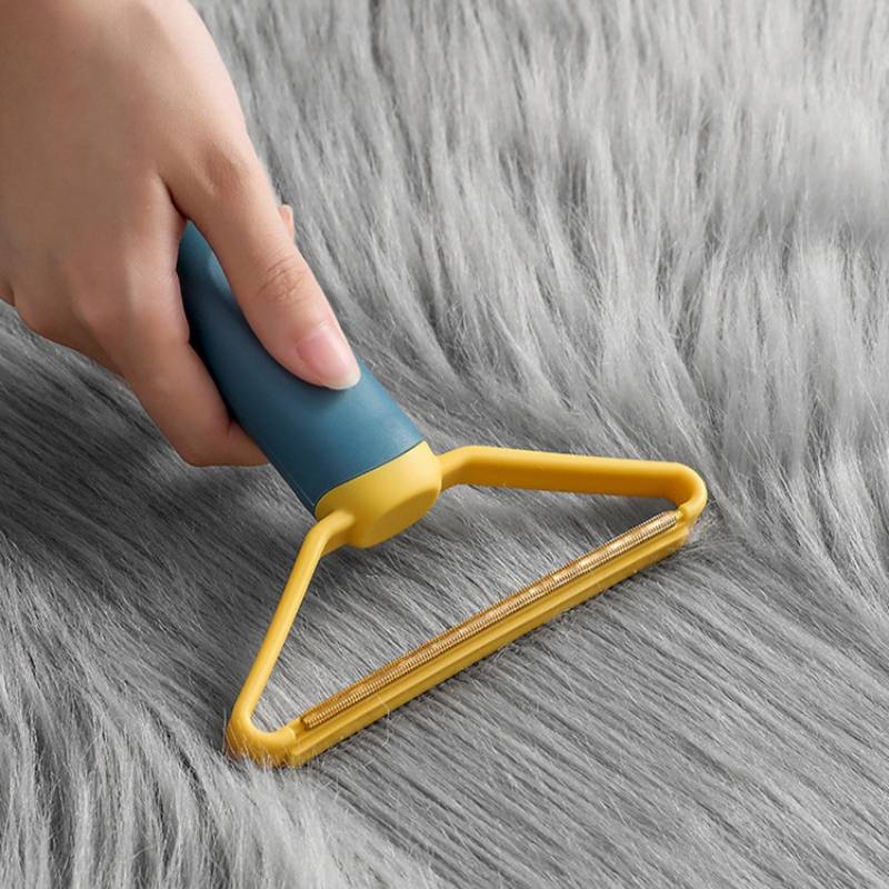 Hand, die eine Fusselrolle auf grauem pelzähnlichem Stoff verwendet, um Tierhaare oder Flusen zu entfernen.