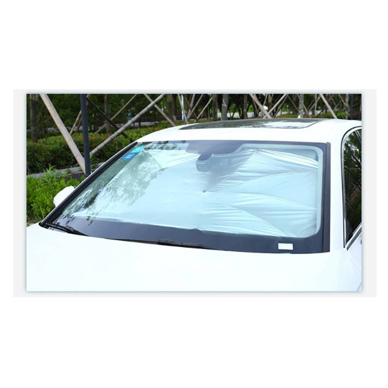 Frontscheibe eines weißen Autos, bedeckt mit einer Sonnenschutzfolie oder Schutzfolie, geparkt im Freien neben Grünflächen und einem Zaun.