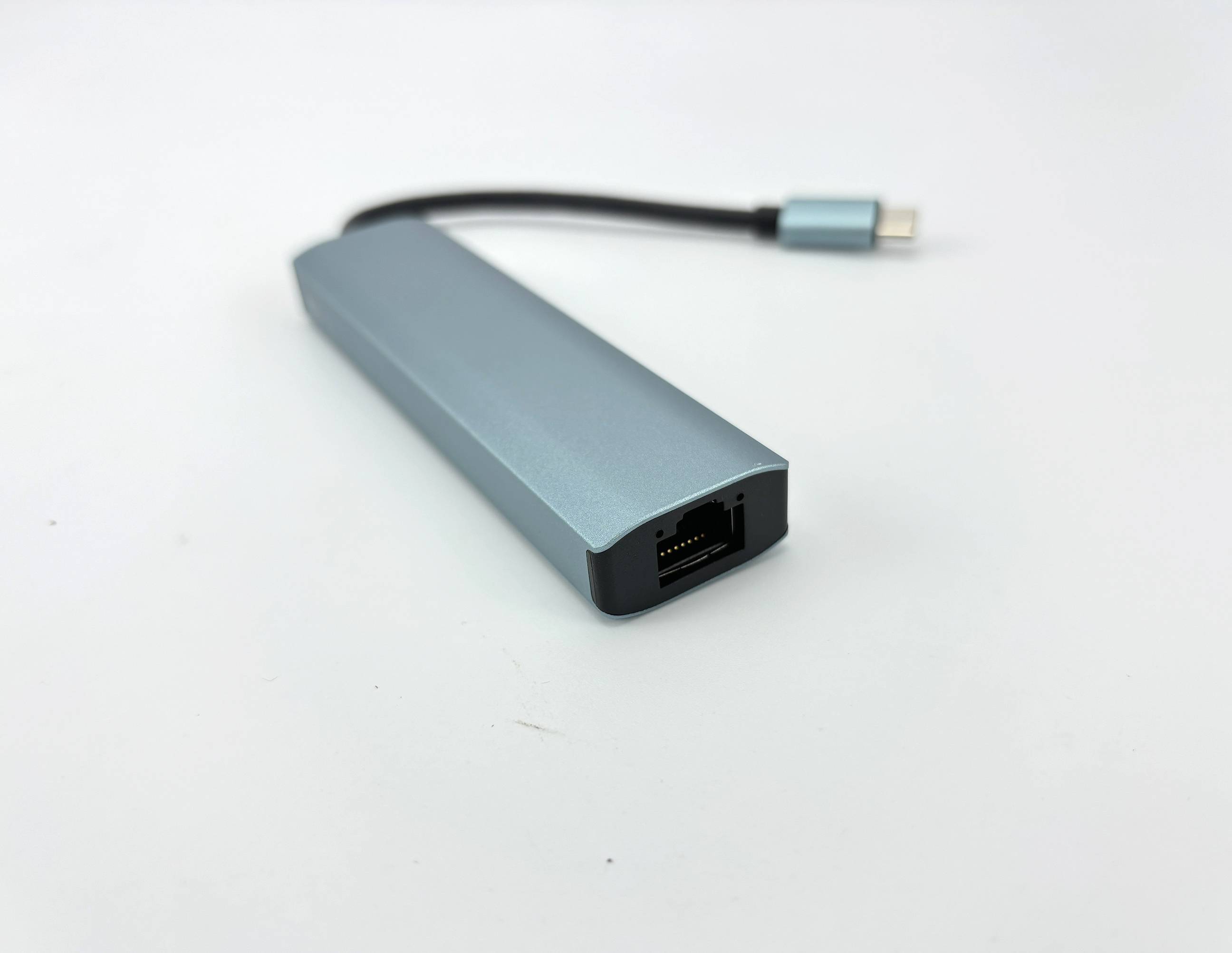 Kleiner silberner USB-C-Adapter oder Hub mit kurzem Kabel und USB-C-Stecker auf weißem Hintergrund.