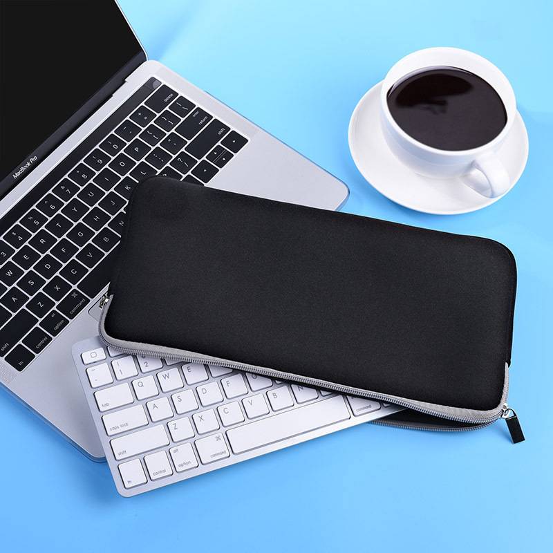 Ein schwarzer Laptop-Schutzbeutel mit Reißverschluss liegt auf einer Laptop-Tastatur neben einer Kaffeetasse auf blauem Hintergrund.