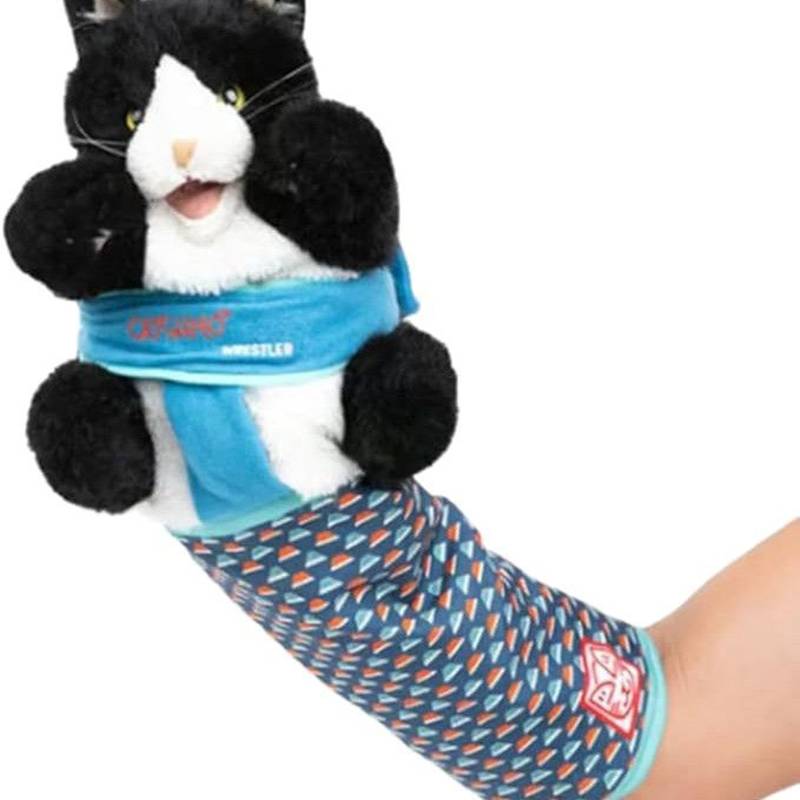 Ein schwarz-weiß-es Plüschkatzentier in einem blauen Hemd und gemustertem Ärmel wird von einem Arm einer Person gegen einen weißen Hintergrund gehalten.