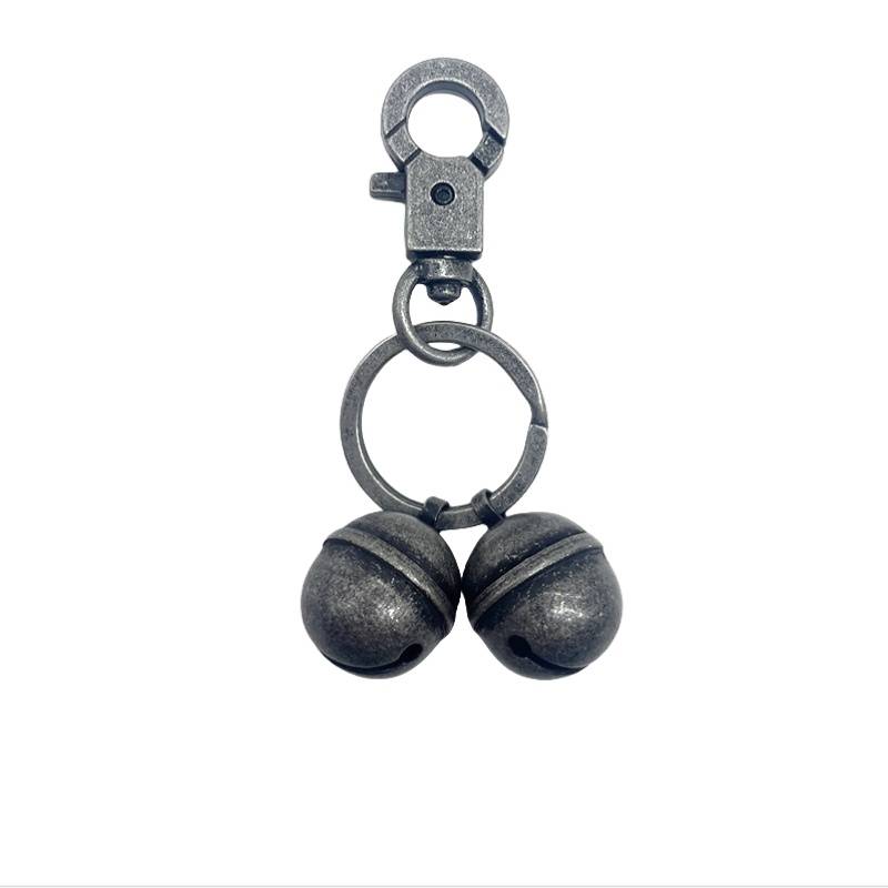 Metallschlüsselanhänger mit drehbarem Karabiner und Spaltring, an dem zwei kleine glöckchenförmige Perlen auf weißem Hintergrund befestigt sind.