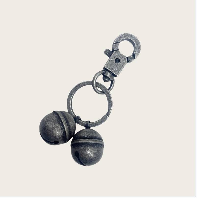 Ein Metallschlüsselanhänger mit zwei dunklen kugelförmigen Glocken oder Anhängern, die an einem Ring und einer Schließe an einem einfachen, hellen Hintergrund hängen.