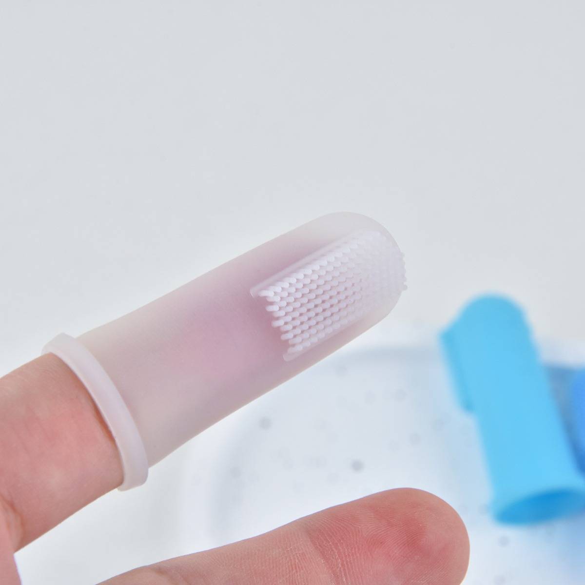 Nahaufnahme einer Fingerspitze, die eine durchsichtige Silikonreinigungskappe mit strukturierten Borsten trägt, die zur Zahn- oder Fingerreinigung verwendet wird.