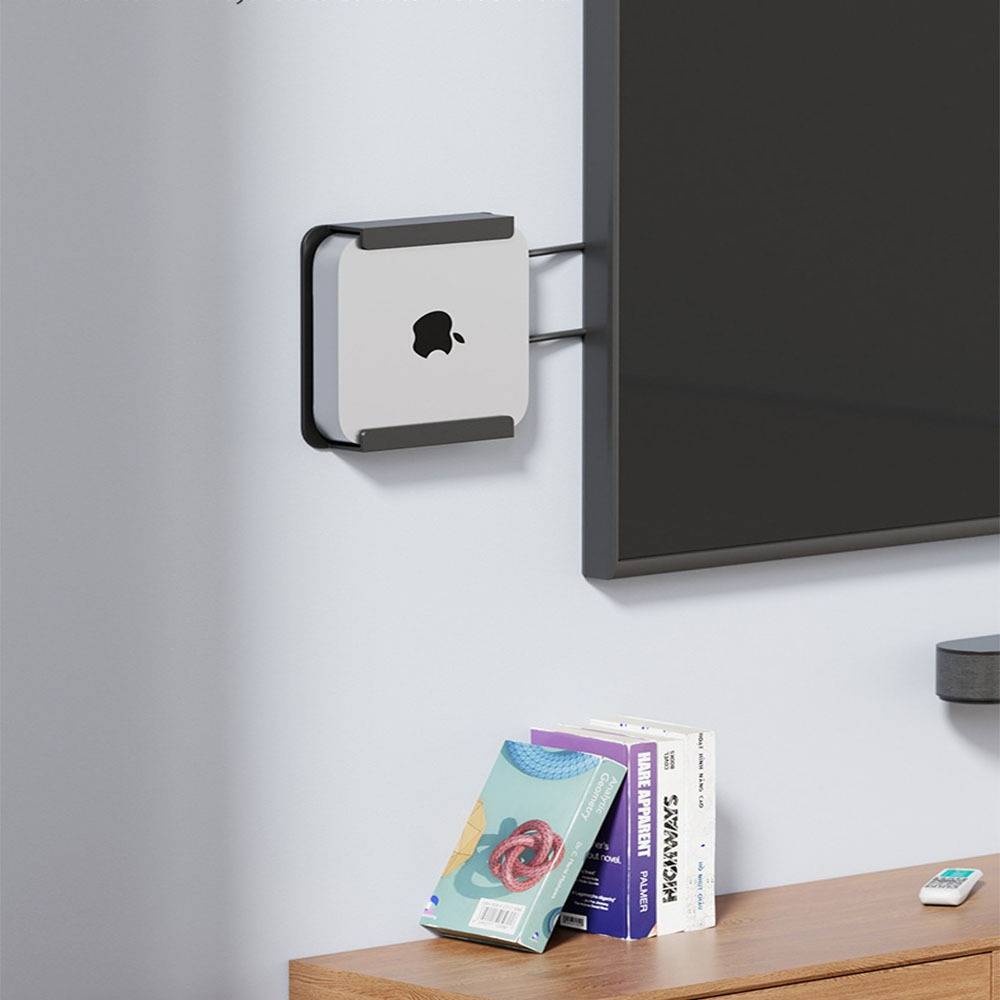 An der Wand montierter Apple-Computer mit Büchern auf einem Schreibtisch unter einem dunklen Monitor und einer kleinen Fernbedienung auf der rechten Seite.