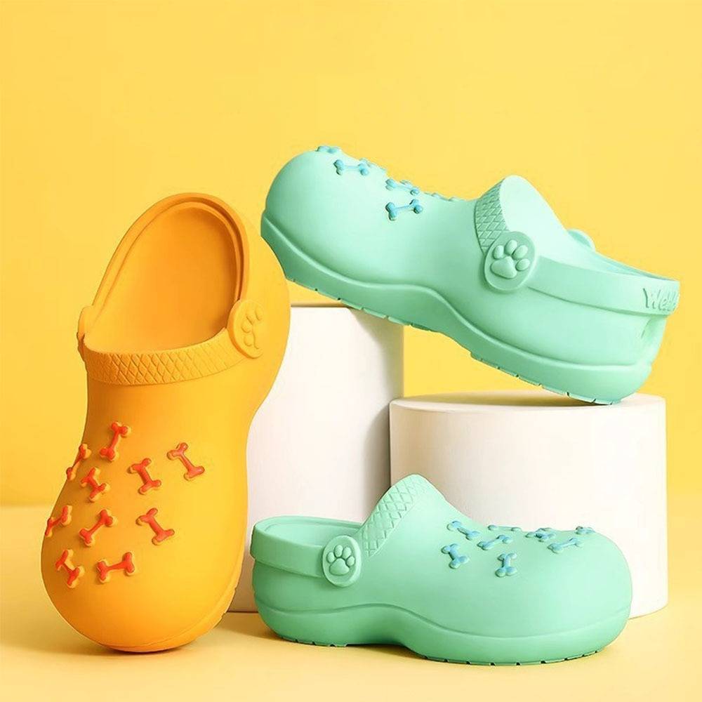 Drei farbenfrohe Clog-ähnliche Sandalen auf weißen Sockeln vor gelbem Hintergrund: eine orange, eine mintgrün aufrecht stehend, eine mintgrün liegend.