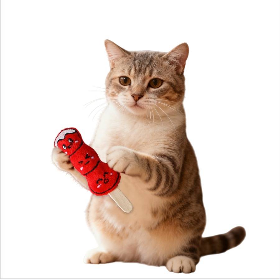 Eine getigerte Katze sitzt und hält ein rotes, cartoon-förmiges Lutschbonbon-Spielzeug vor einem einfachen weißen Hintergrund.