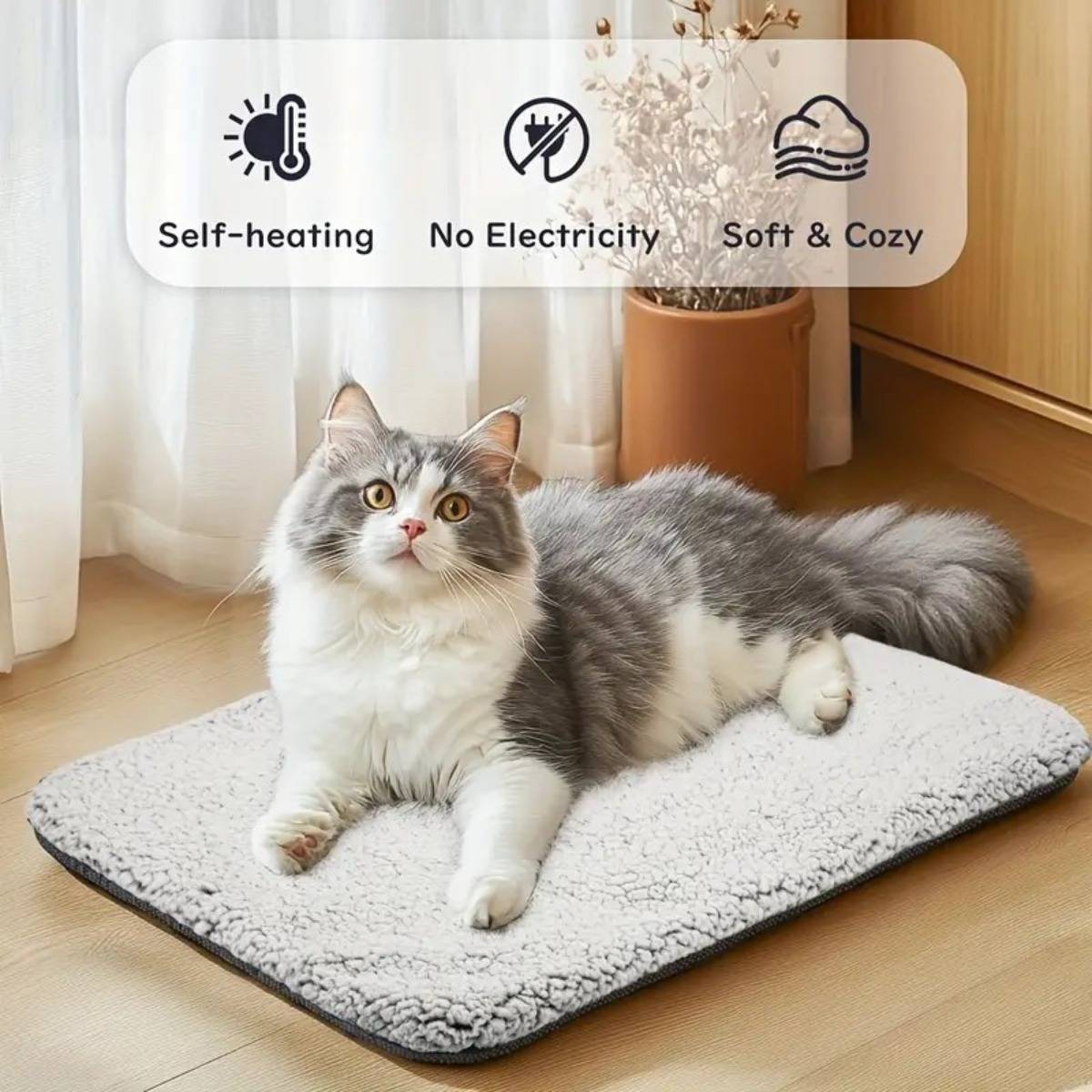 Grau-weiße Katze, die auf einer selbstwärmenden, stromlosen, weichen und gemütlichen Haustiermatte im Innenbereich liegt, mit Funktionssymbolen und Beschriftungen oben.