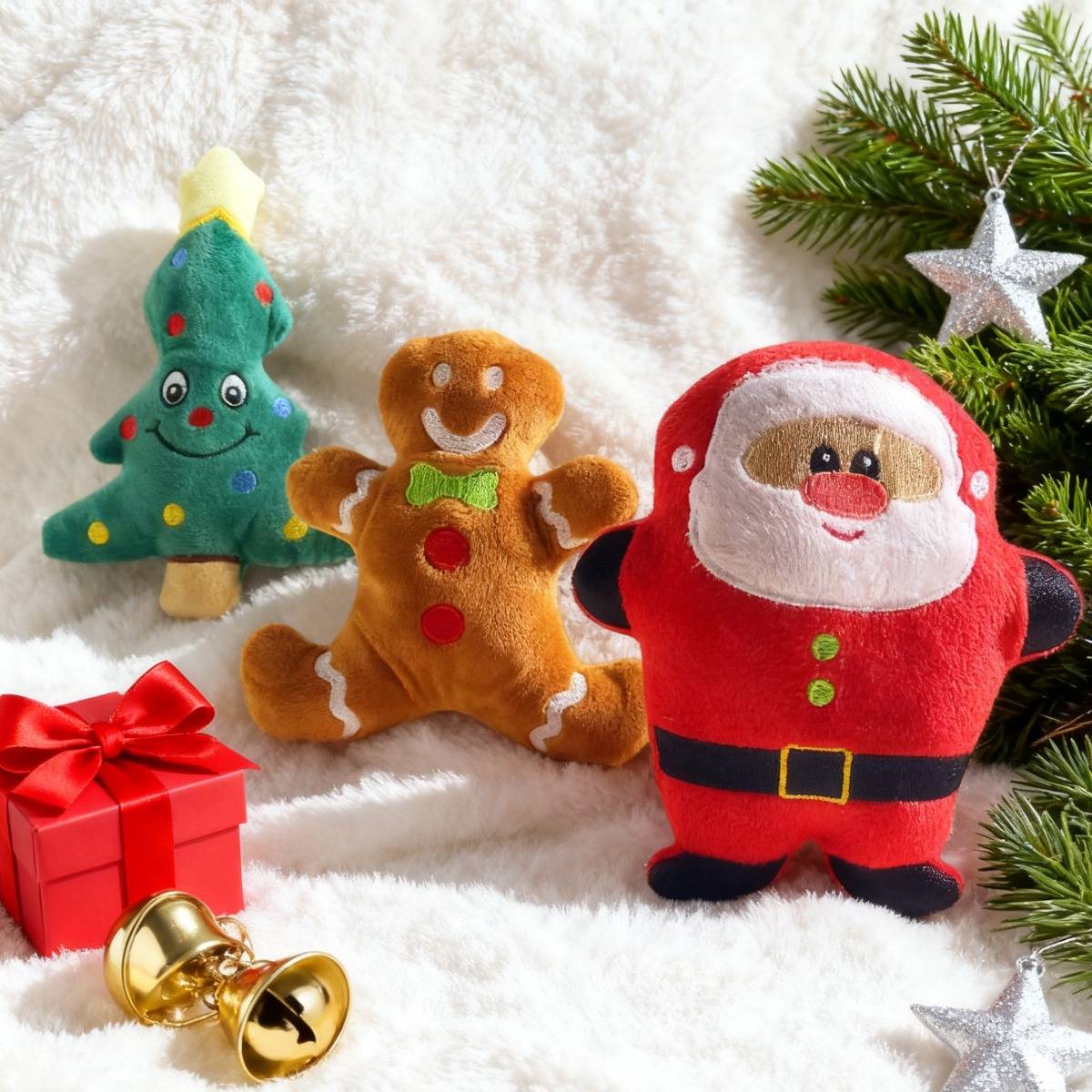 Weihnachtsplüschtiere in Form eines Baumes, eines Lebkuchenmanns und eines Weihnachtsmanns neben einem eingewickelten Geschenk, Glocken und immergrünen Zweigen.