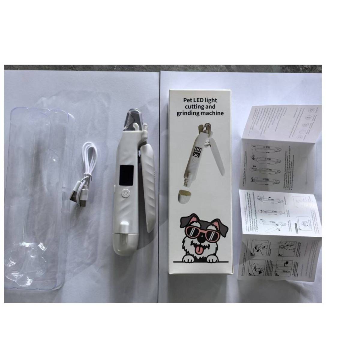 Heimtier-LED-Nagelschneider-Set mit Schneidern, USB-Kabel, Karton und Bedienungsanleitungen auf einem Tisch ausgelegt.