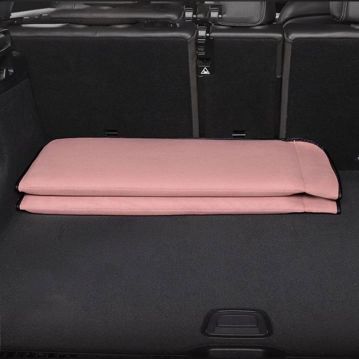 Zusammengeklapptes rosafarbenes Matratzen-Kissen flach im Kofferraum eines Autos liegend, mit hochgeklappten Rücksitzen.