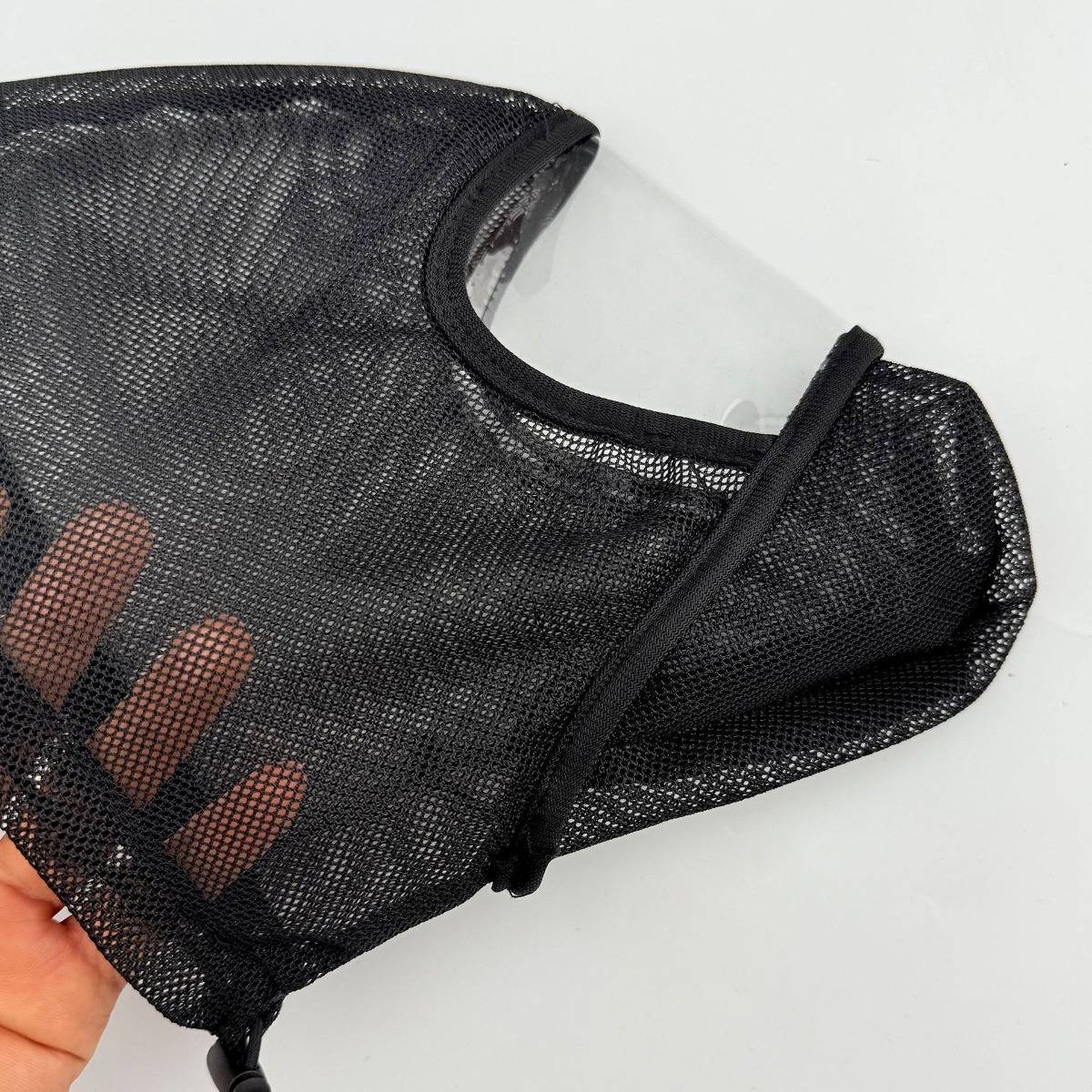 Schwarze Schutzgesichtsmaske aus Maschengewebe mit klarer Kunststoffschutzbrille, in einer Hand vor weißem Hintergrund gehalten.