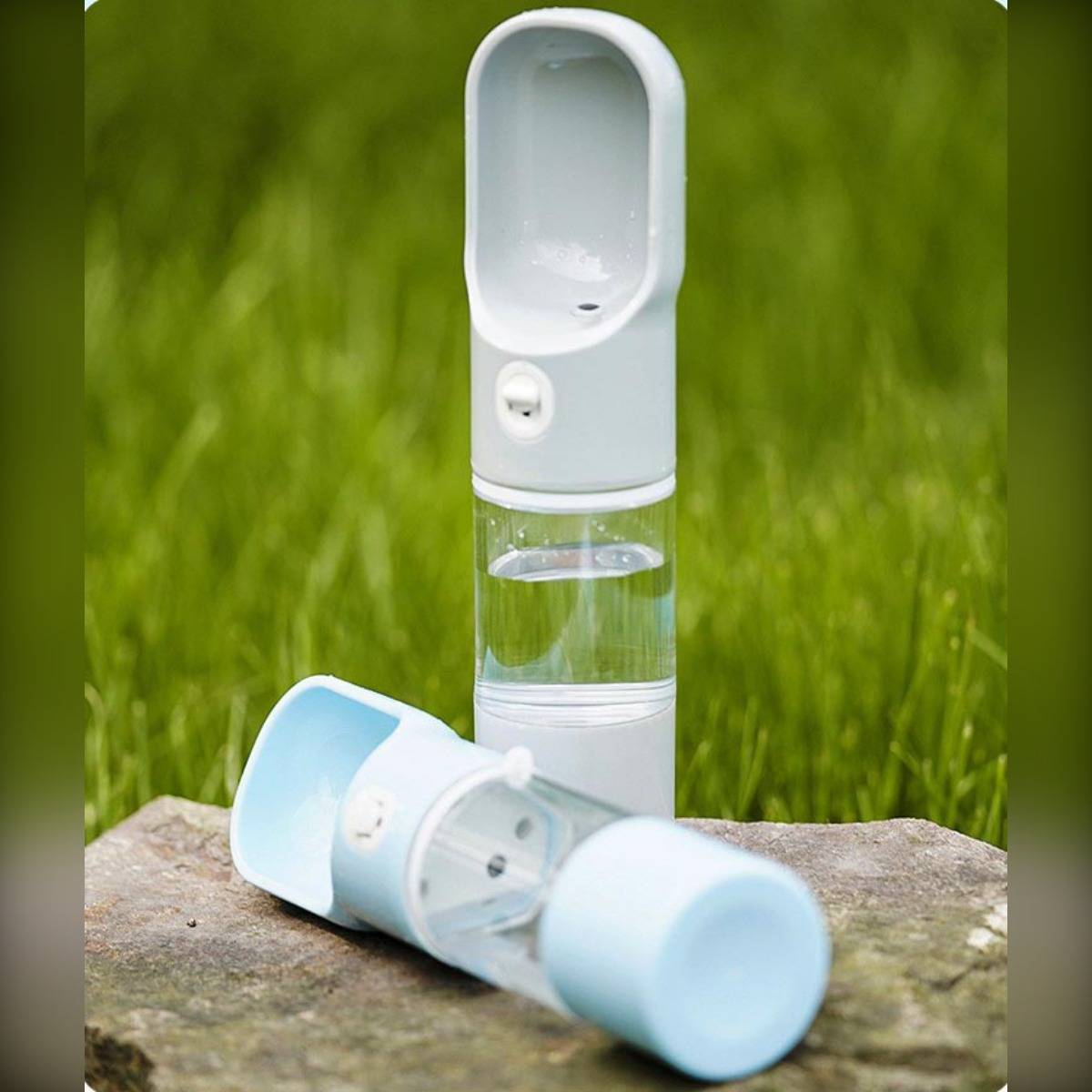 Zwei tragbare Sprühventilatoren auf einem Stein im Gras, einer aufrecht stehend und einer liegend, mit durchsichtigen Wasserbehältern.