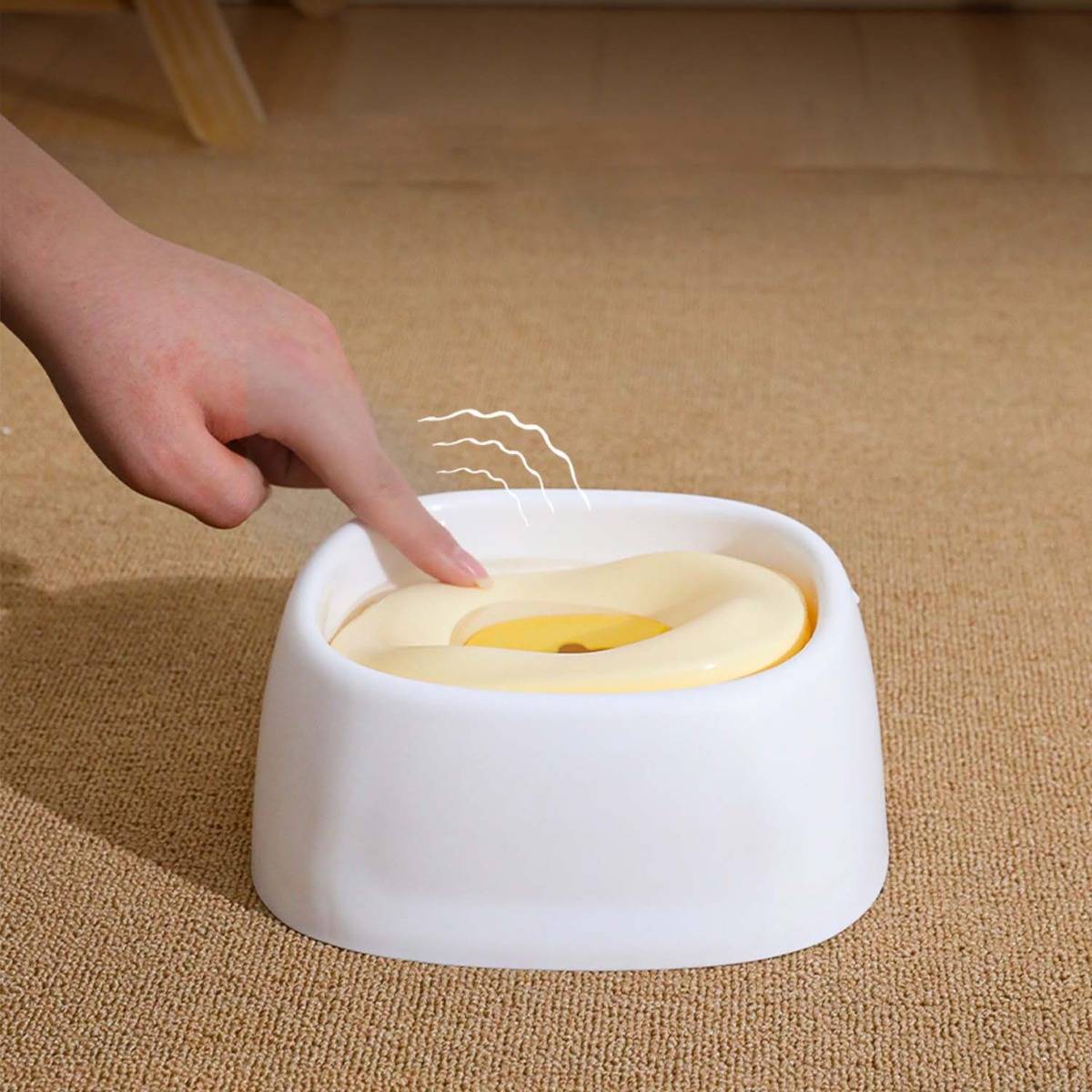 Hand drückt eine weiße Haustierwasserfontäne auf einen Teppich, wobei Wellenringe auf der Oberfläche zeigen, dass das Zentrum aktiviert ist.