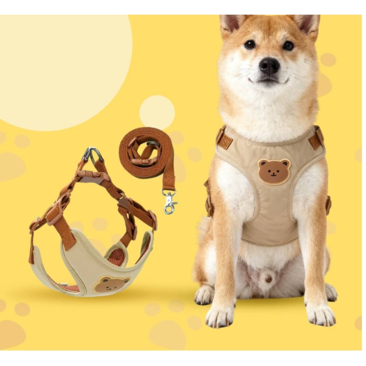 Shiba Inu in einem beigen Geschirr mit Bärenmotiv, zusammen mit passendem Geschirr und Leine auf gelbem Hintergrund dargestellt.