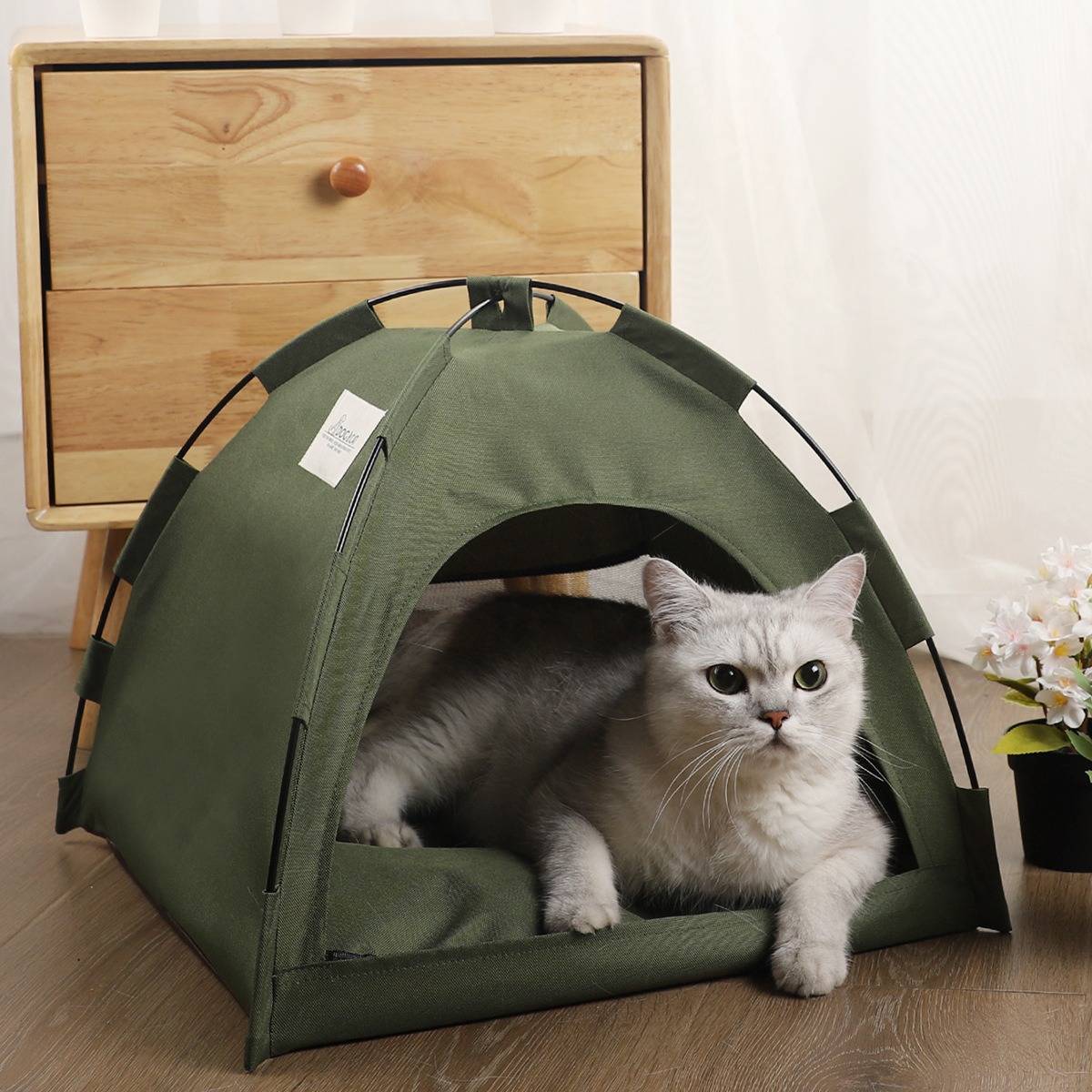 Eine weiße Katze ruht sich in einem grünen zeltartigen Haustierbett auf einem Holzboden aus, mit einem kleinen Schrank und Blumen im Hintergrund.
