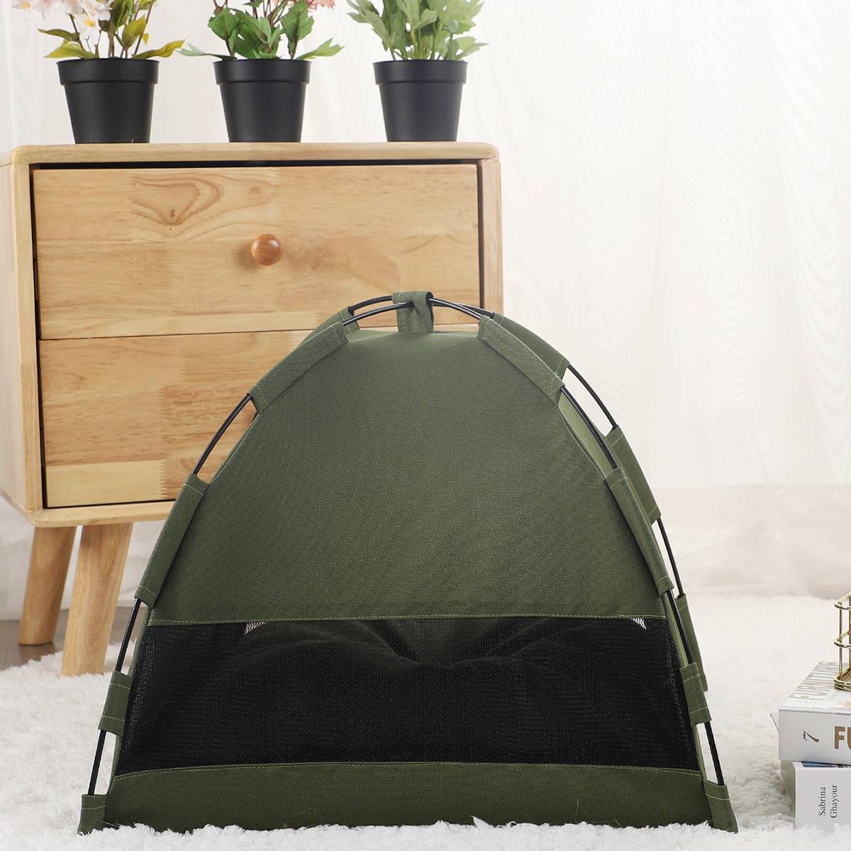 Olivgrünes Pop-up-Haustierkabinett mit schwarzem Mesh-Front, in Innenräumen auf einem weißen Teppich neben einem Holzschrank und Topfpflanzen gezeigt.