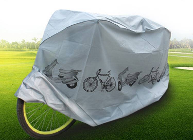 Fahrrad mit grauer Regenschutzhülle mit Roller- und Fahrradillustrationen, auf Gras im Freien geparkt.