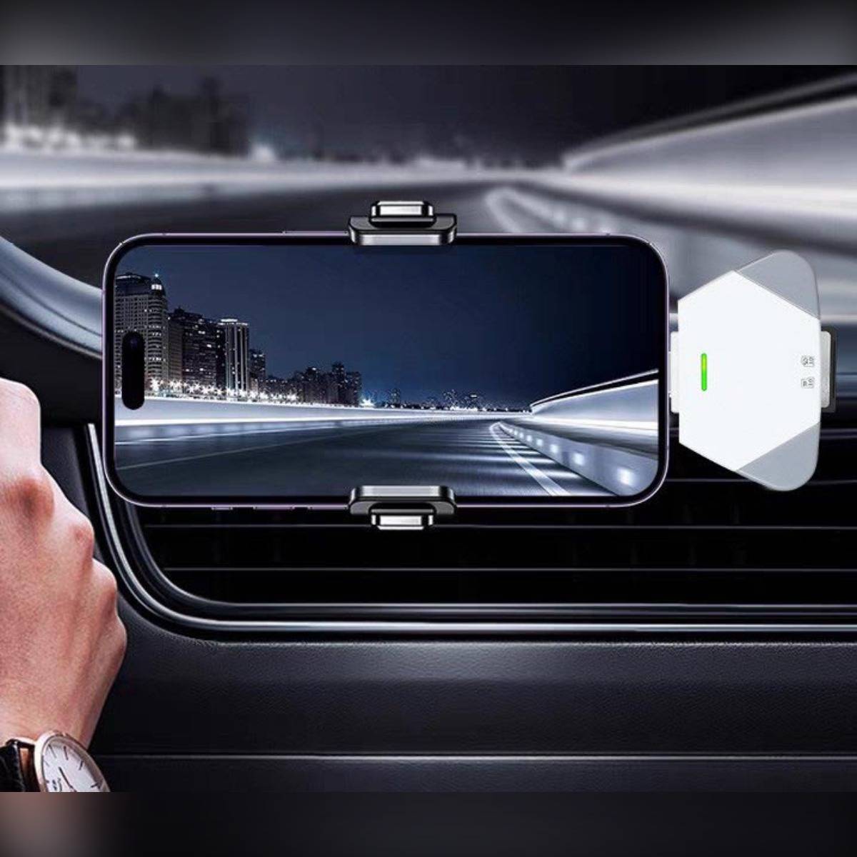 Auf dem Armaturenbrett eines Autos montiertes Smartphone zeigt eine nächtliche Straßenszene, mit einem kleinen weißen Gerät daneben befestigt, was auf Navigation im Auto oder Fahrassistenz hindeutet.
