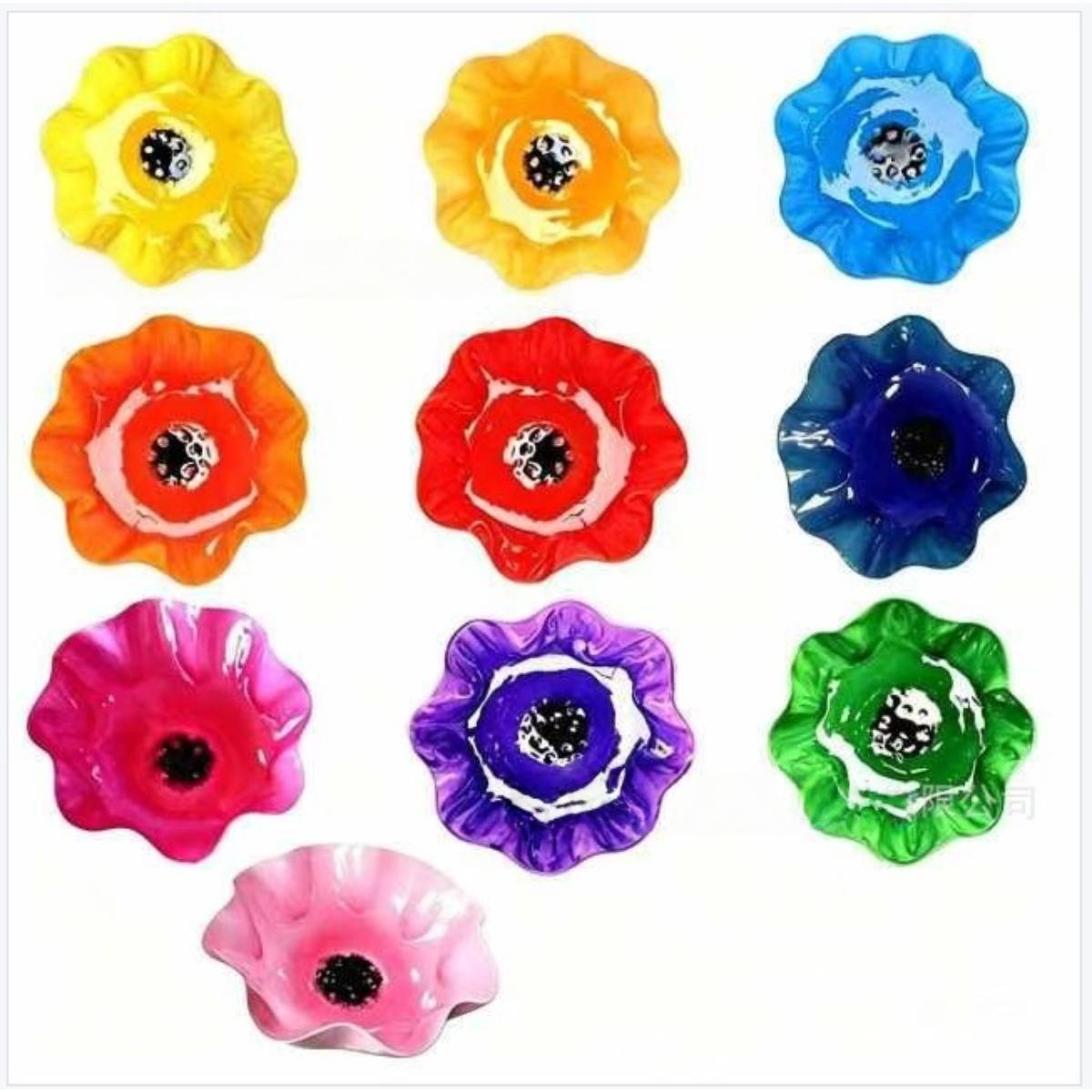 Bunte blütenförmige Glaskugeln in Gelb, Orange, Blau, Rot, Rosa, Lila und Grün auf weißem Hintergrund angeordnet.