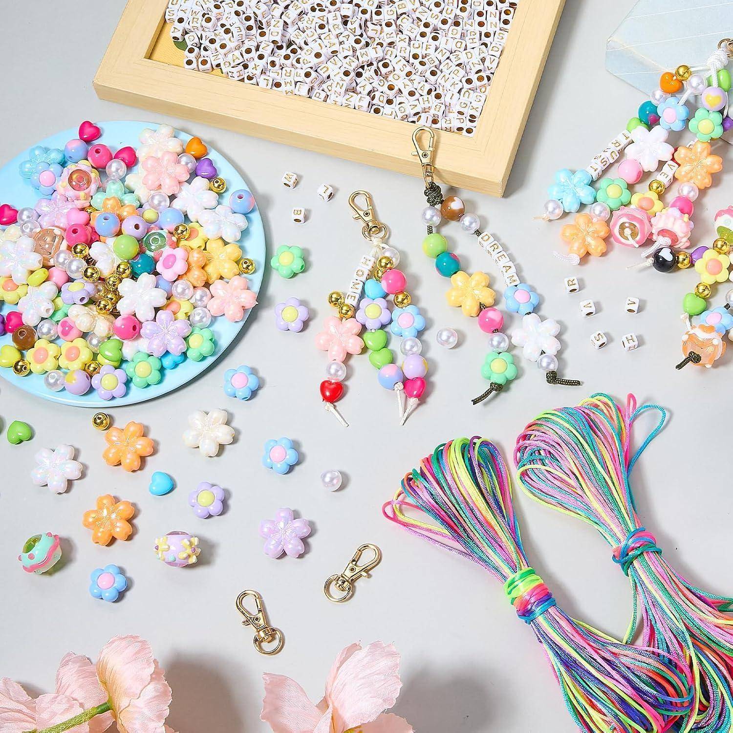 Bunte handgefertigte Bastelmaterialien und fertige Accessoires auf einem Tisch: Blumenperlen, Schlüsselanhänger, Anhänger und Regenbogenkordeln zum Schmuckmaking.