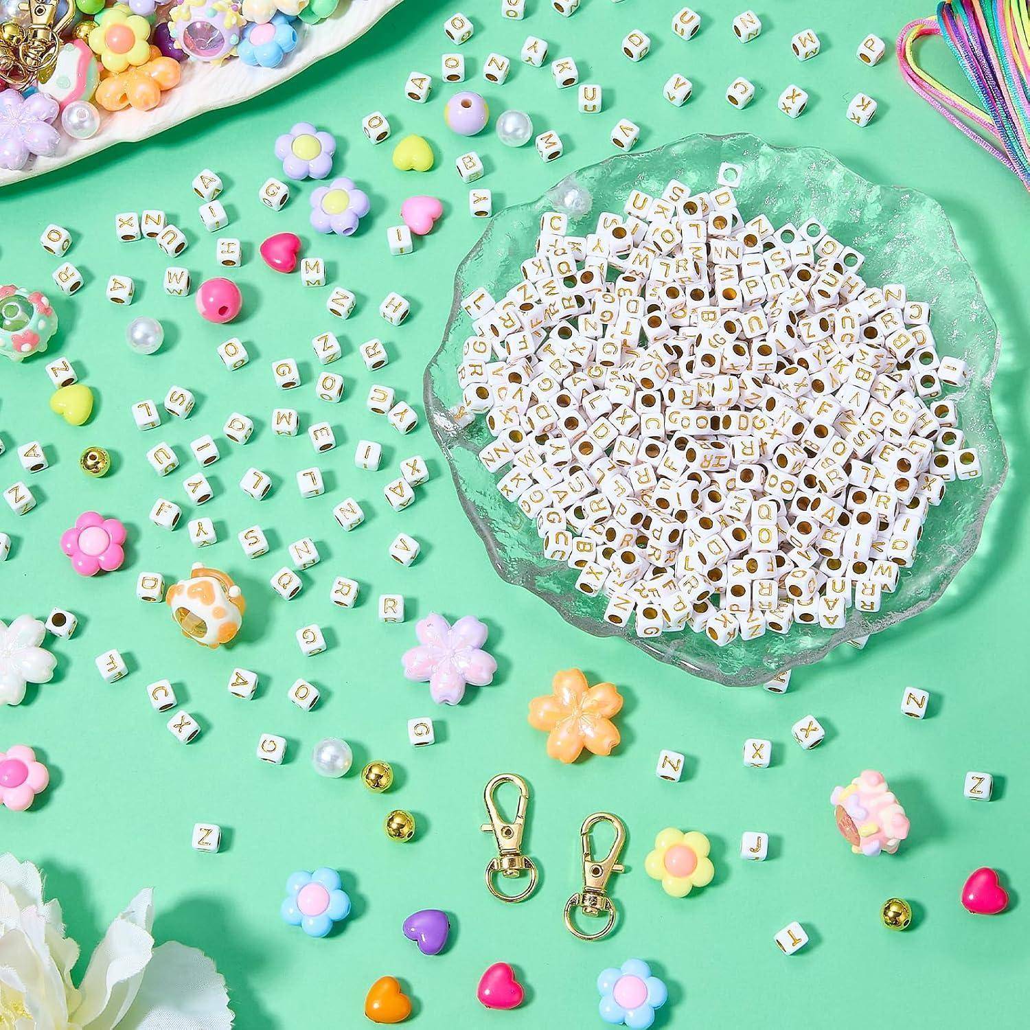 Aufsicht von Bastelmaterialien: eine Schüssel mit Alphabet-Perlen, verstreute Buchstabenkacheln und bunte Blumenanhänger auf mintgrünem Hintergrund.