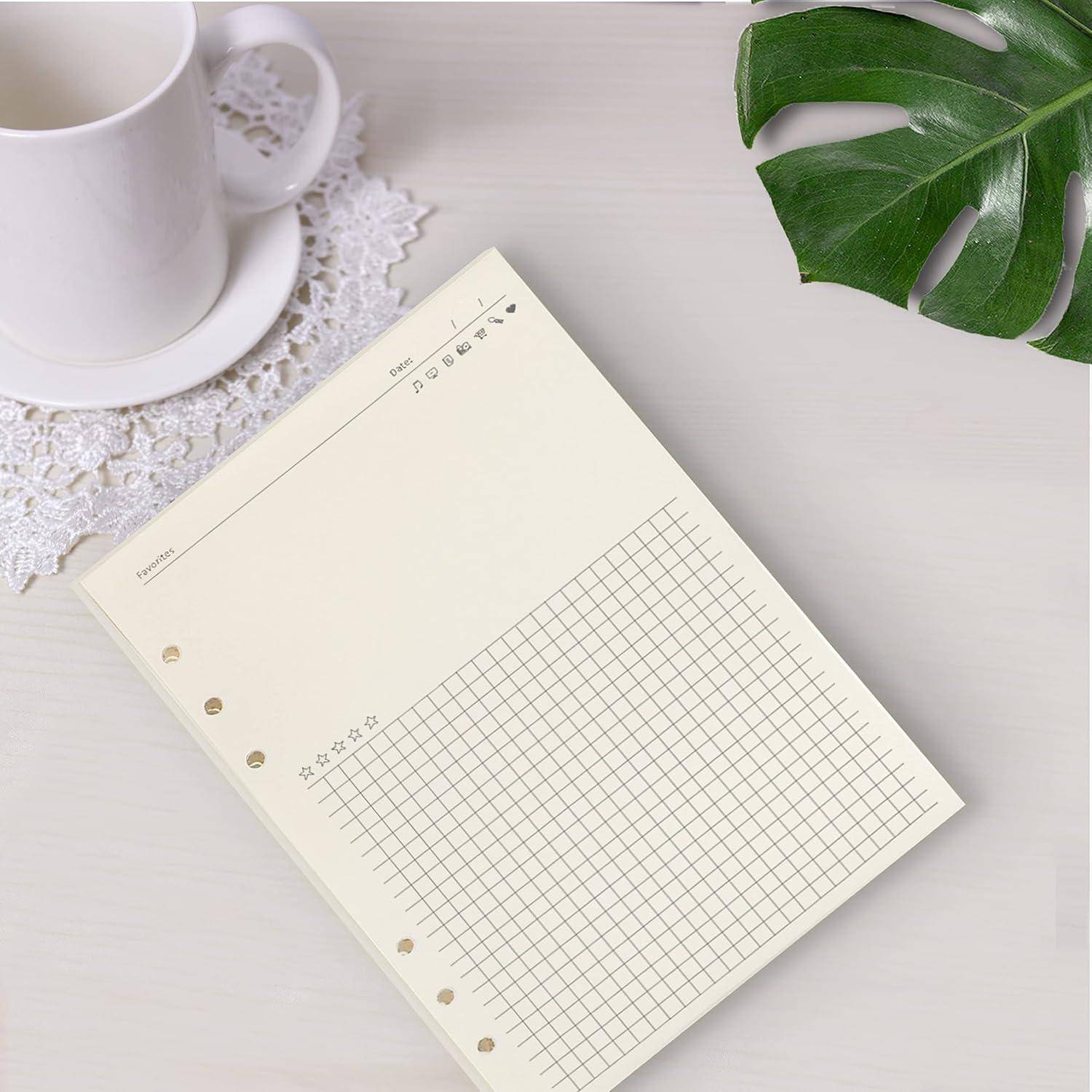 Leeres Notizbuch-Gitter auf einem Schreibtisch neben einer Tasse, einer Spitzenuntersetzer und einem grünem Blatt, das ein minimalistisches Schreibwaren-Layout zeigt.