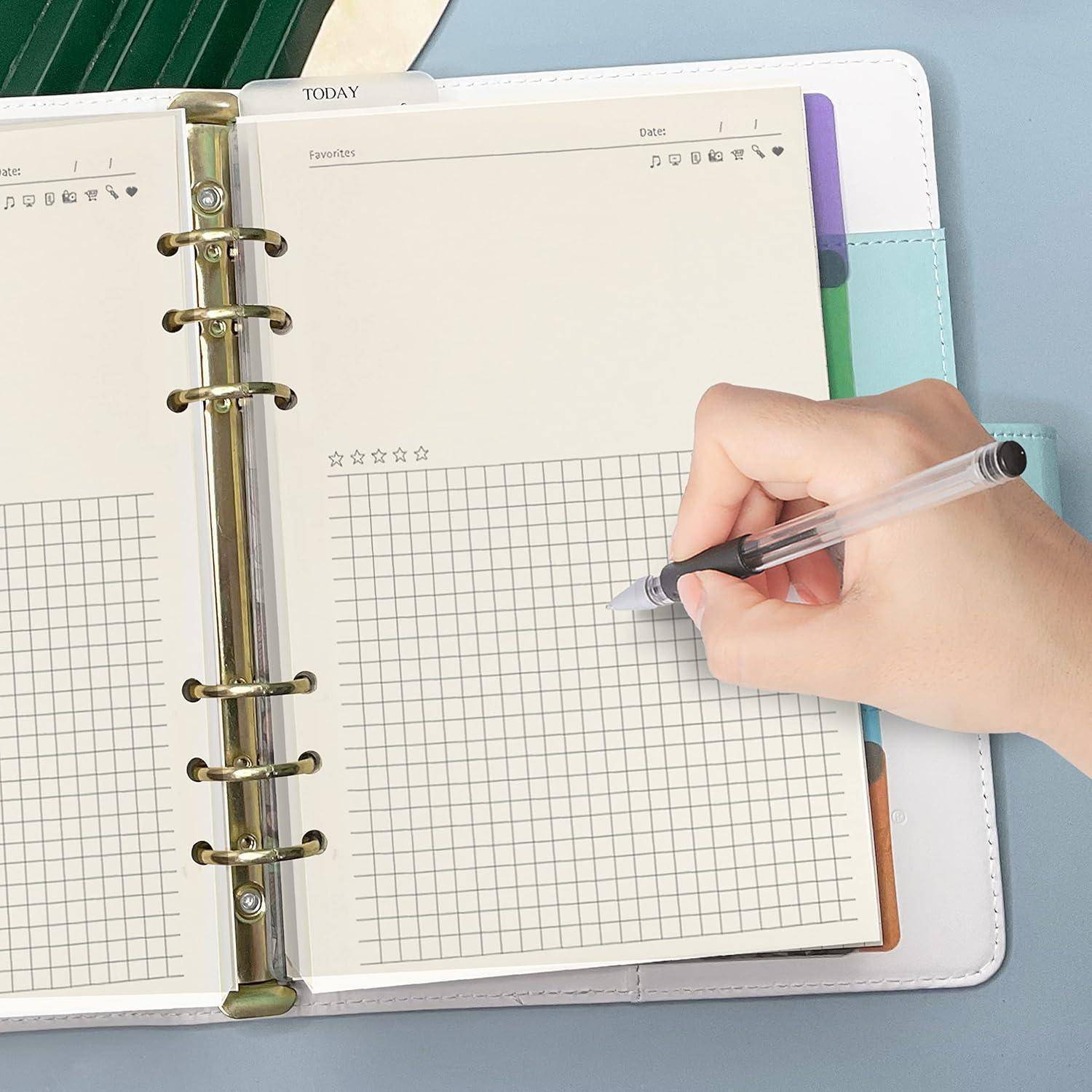 Hand schreibt in einem karierten Planernotizbuch mit Ringbinder und farbigen Trennblättern, die darunter sichtbar sind.