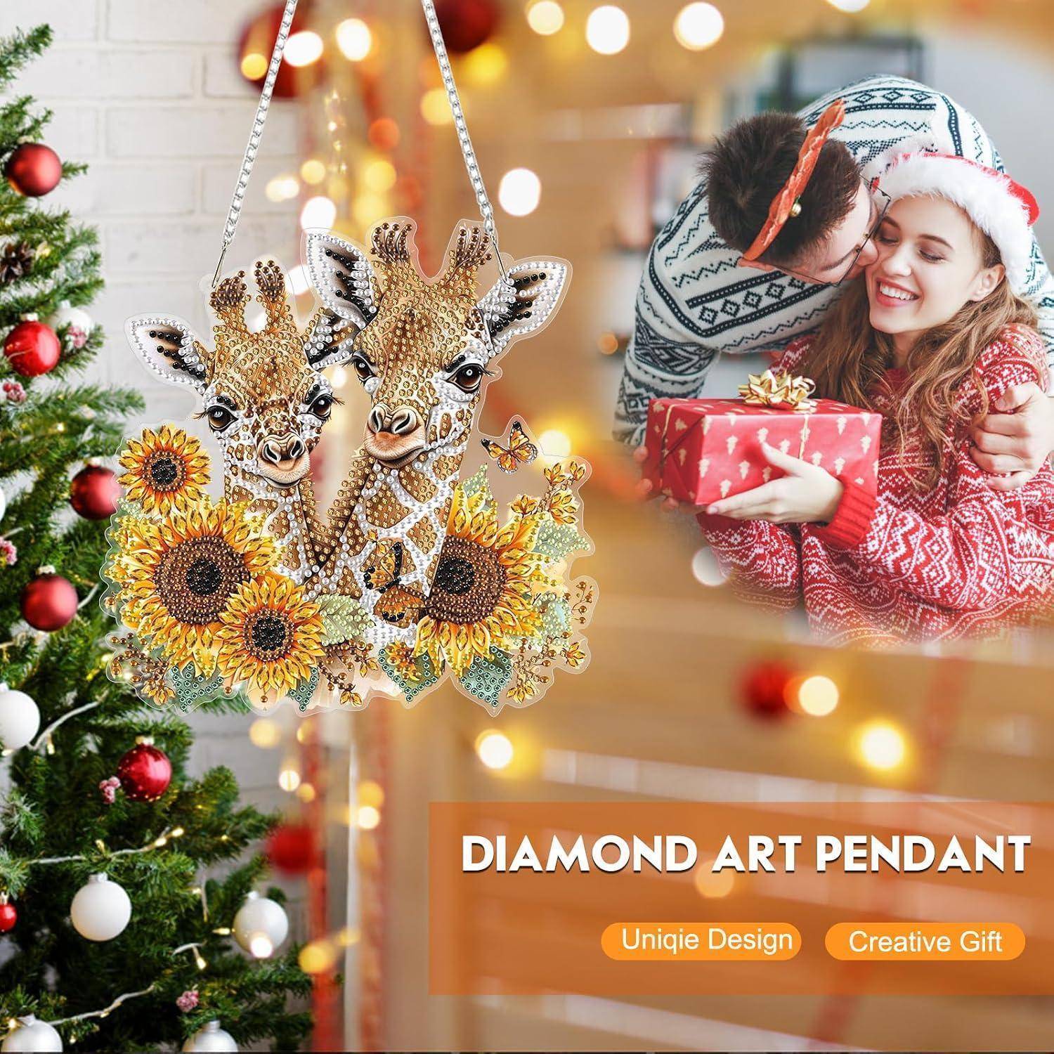 Werbebild eines Diamant-Kunstanhängers mit zwei Giraffen und Sonnenblumen, neben einem lächelnden Paar, das neben einem geschmückten Baum ein Weihnachtsgeschenk austauscht.
