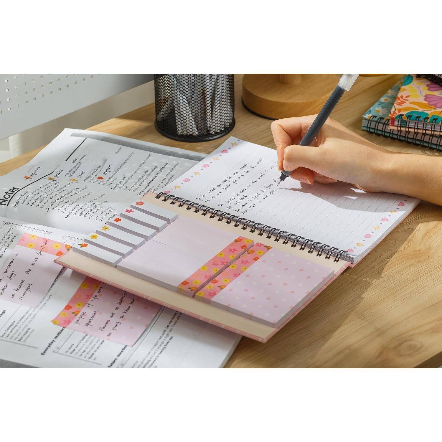 Handschriftliche Notizen in einem Spiralplaner auf einem Schreibtisch neben gedruckten Arbeitsblättern und Schreibwaren.