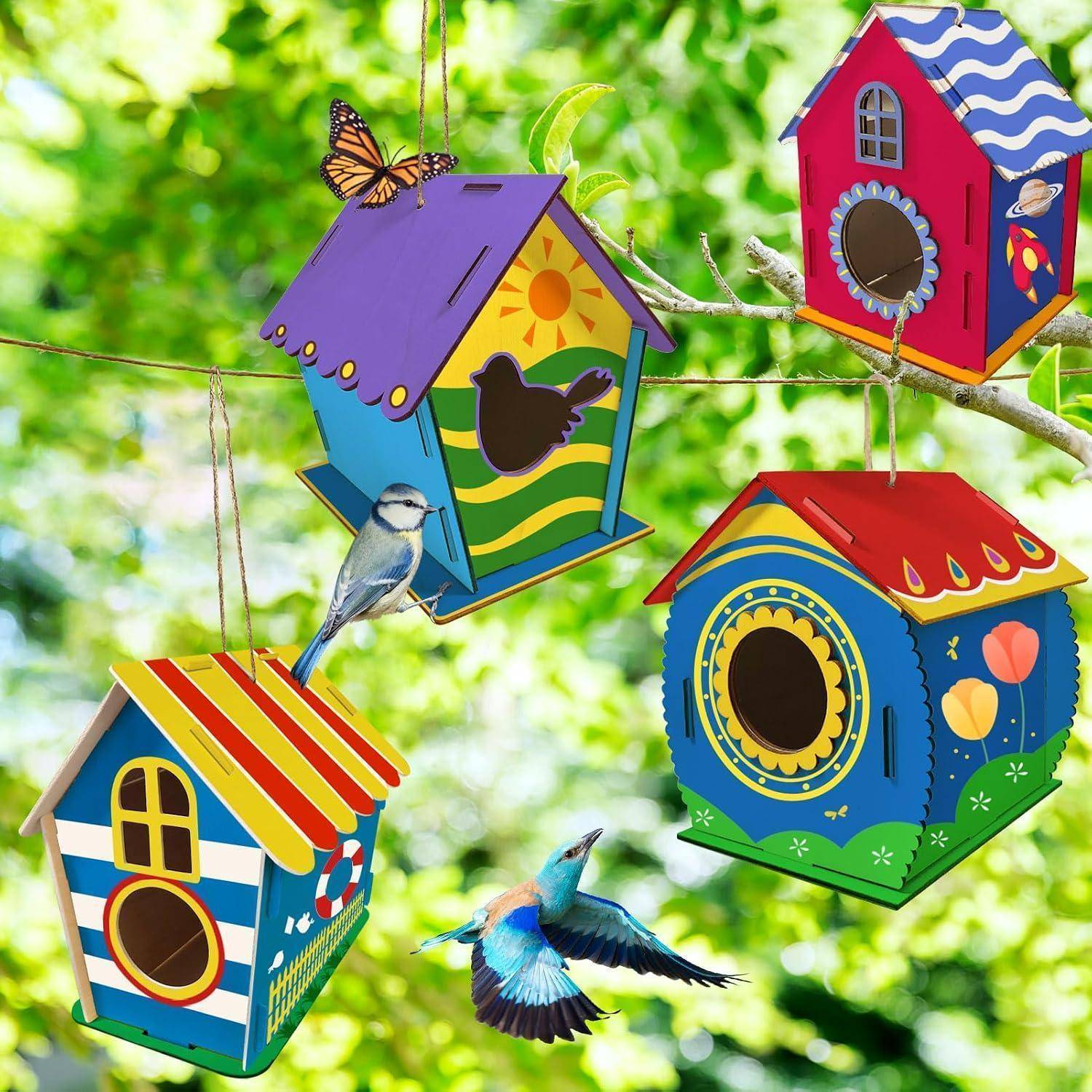 Bunte hängende Vogelhäuser an Baumästen mit zwei kleinen Vögeln und einem Schmetterling vor einem unscharfen grünen Hintergrund.