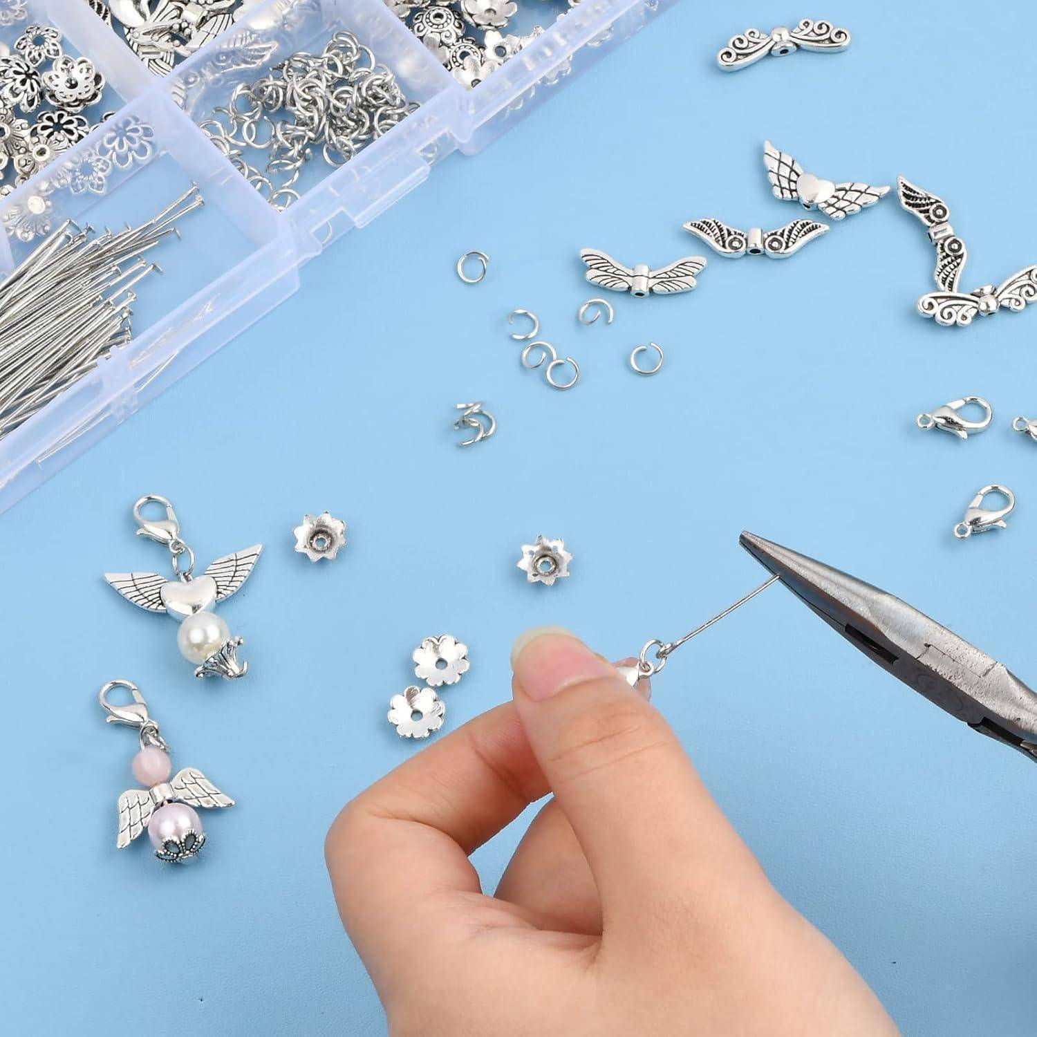 Das Handfertigen eines silbernen geflügelten Charms mit einer Zange auf einer blauen Oberfläche, mit Perlenarbeits- und Schmuckteilen in einem Kunststofforganizer in der Nähe.