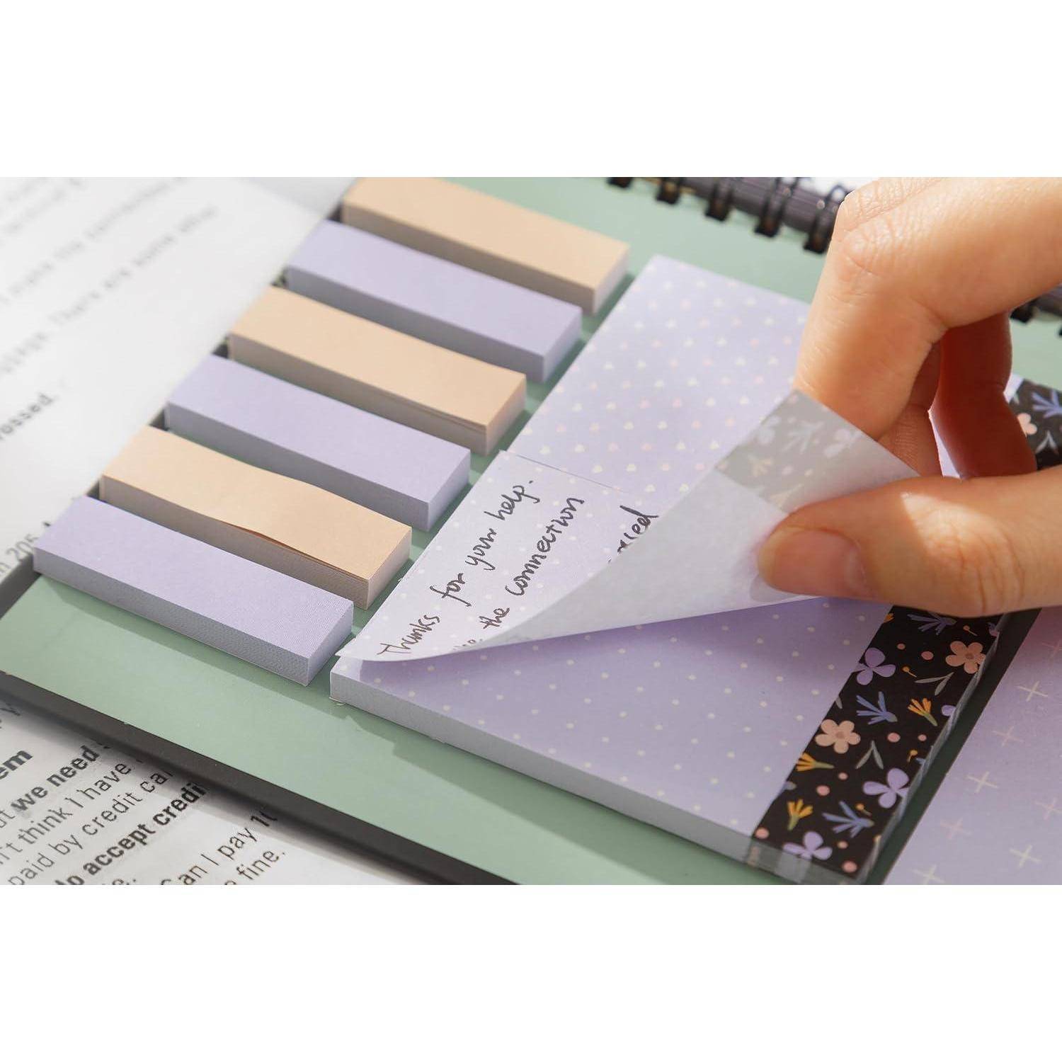 Hand schlägt einen violetten Klebezettel mit „Danke für deine Hilfe, bis morgen!" auf einem pastellfarbenen Notizbloack mit Registern zurück.