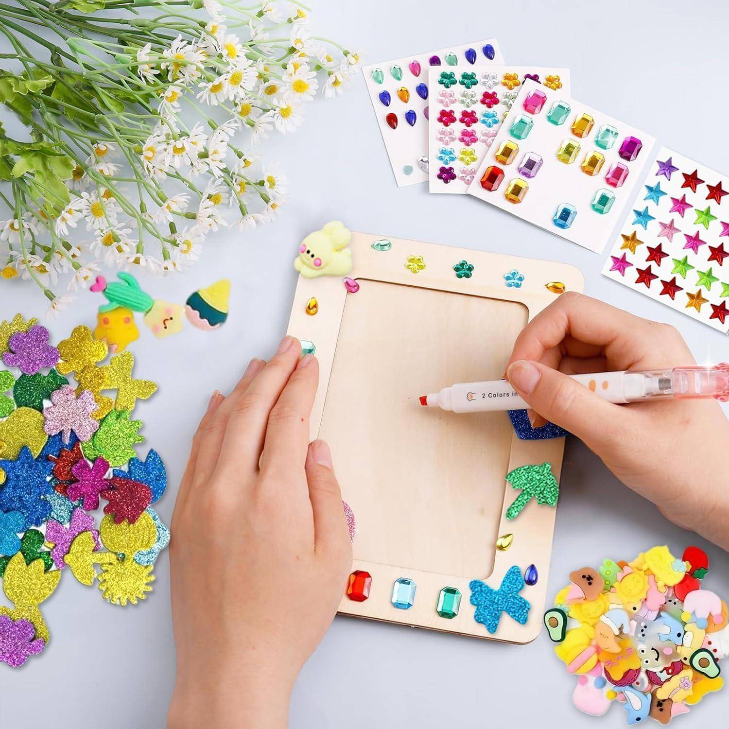 Hände, die einen hölzernen Bilderrahmen mit einem Stift und bunten Aufkleberjuwelen verzieren, mit sortierten Bastelaufklebern, die herum verteilt sind.