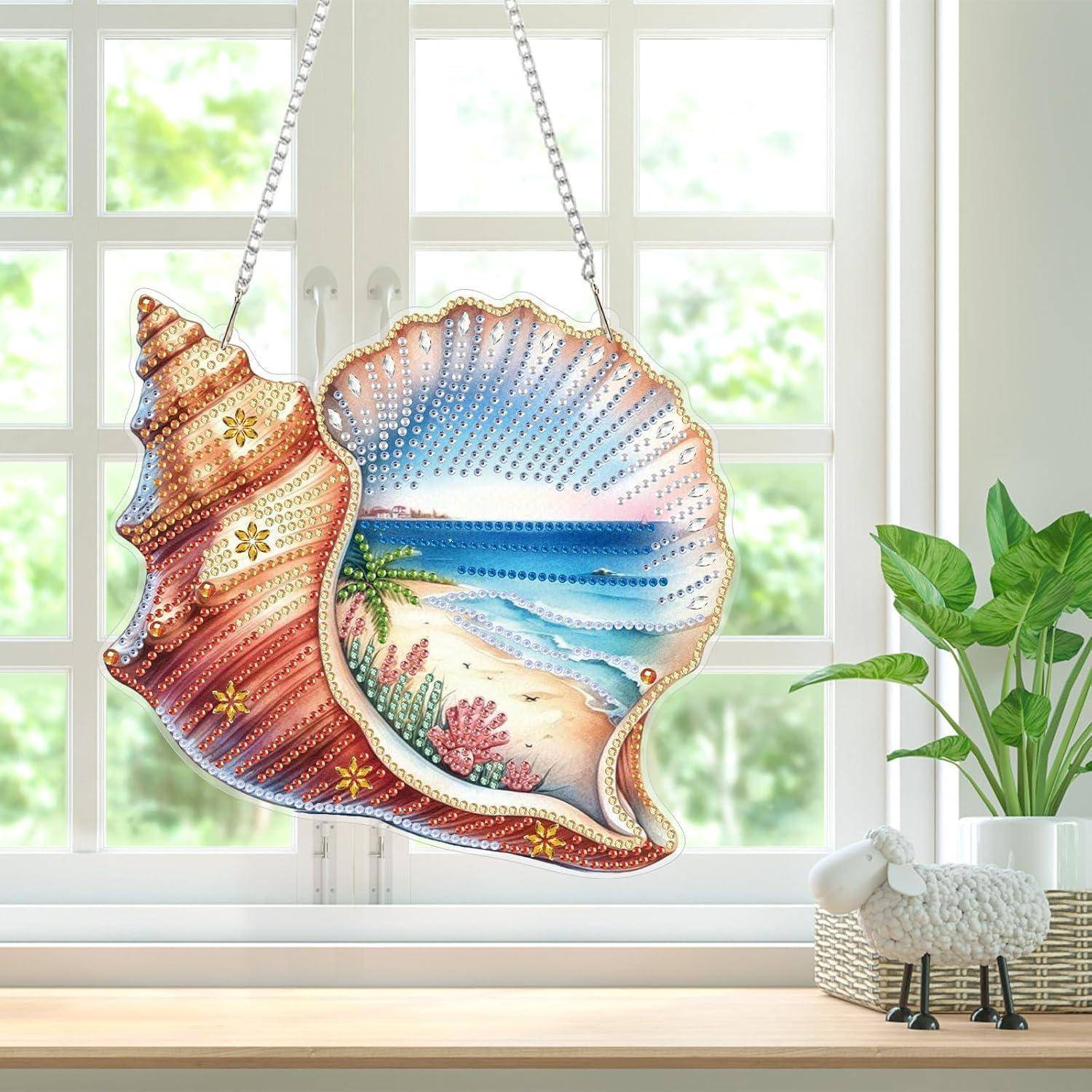 Dekorative muschelförmige Wandkunst zum Aufhängen mit einer bemalten Strandszene, ausgestellt vor einem Fenster neben einer Topfpflanze und einer Schaffigur.