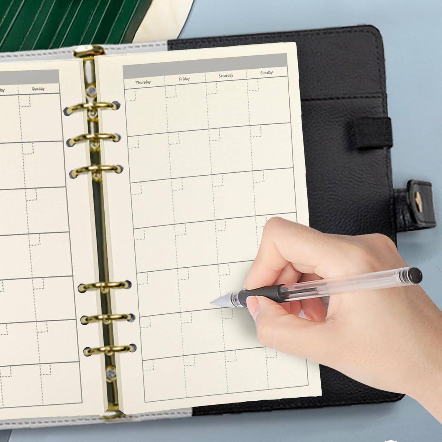 Handschrift in einem spiralgebundenen Plankalender mit leeren Wochenkästchen; ein schwarzes Notizbuch liegt darunter.