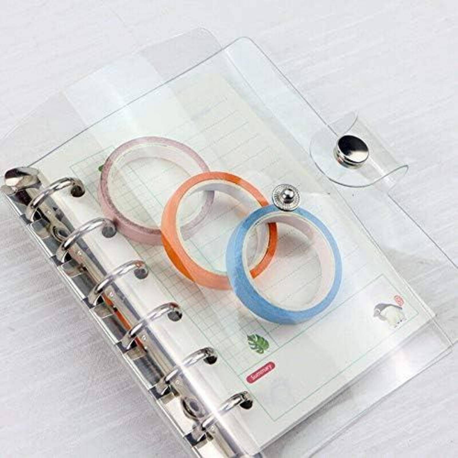 Transparenter Ringordner-Planer mit durchsichtigen Deckeln und pastellfarbigen Washi-Tape-Rollen oben.