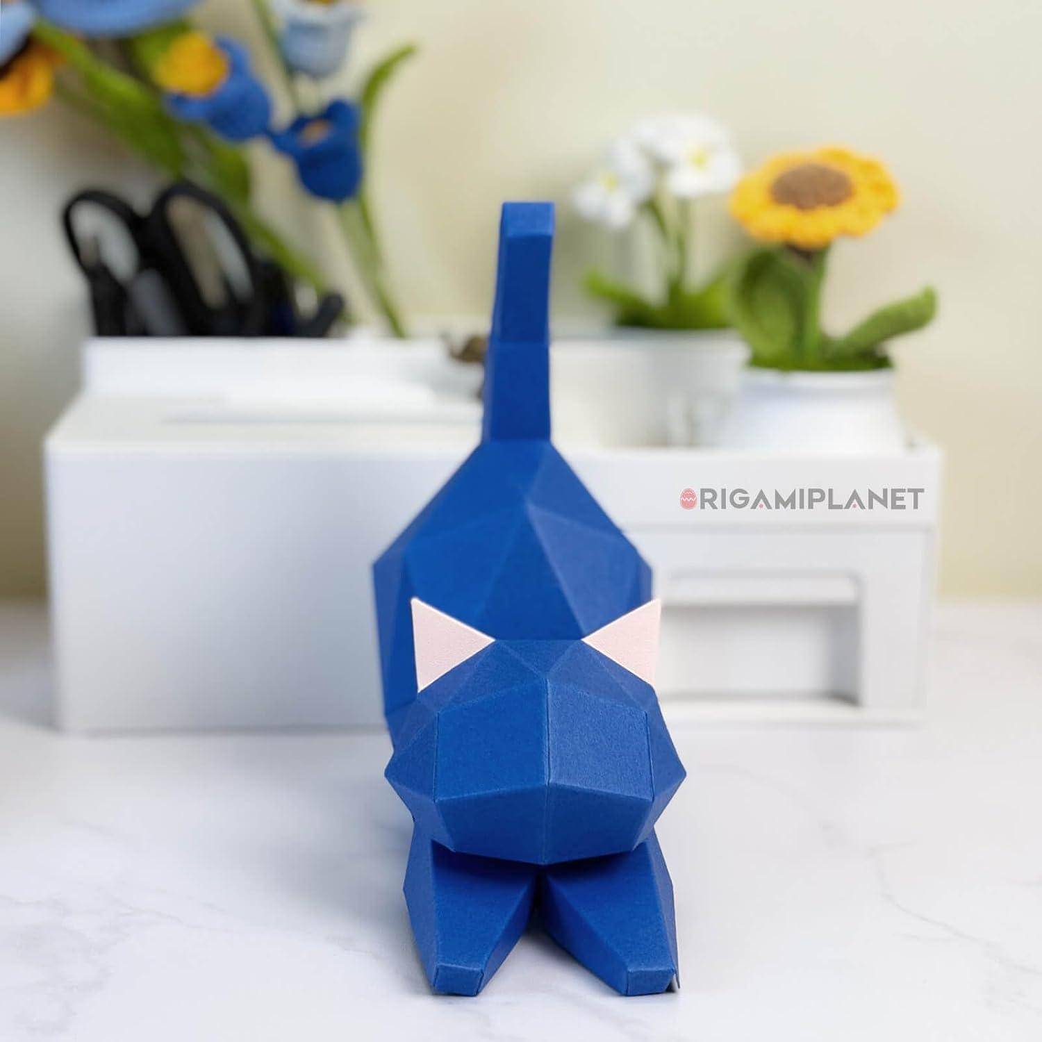 Blaues geometrisches Papiertiermodell, das auf einem Tisch steht, mit unscharfen Blumen und Schere im Hintergrund.