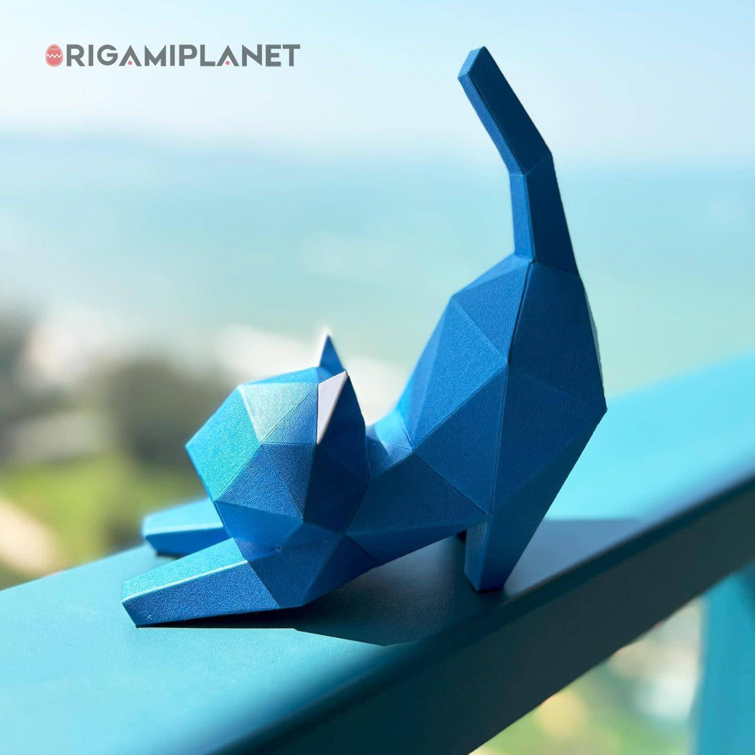 Blaue geometrische Katzenfigur, die sich auf einem Geländer streckt, mit unscharfem Außenhintergrund und dem Logo „RIGAMI PLANET" in der Ecke.